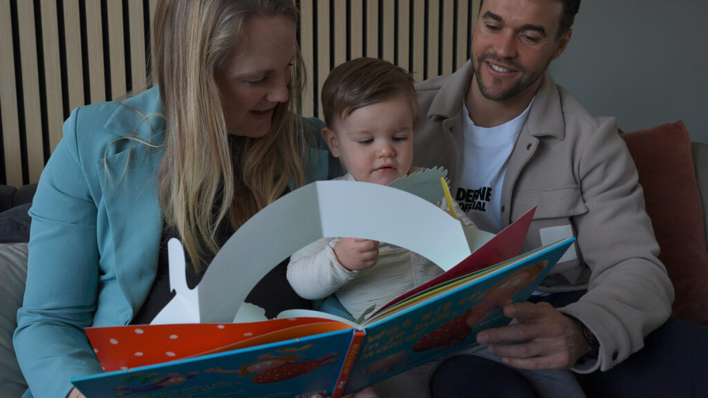 Twee ouders lezen een boekje voor aan hun zoon. Dit wordt vastgelegd op film.